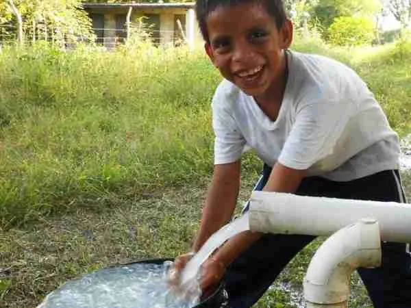 Boy washing hands in bucket smiling